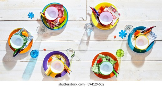 Colorful Picnic Table Place Settings With Empty Multicolored Plates And Bowls, Glasses And Flower Decals For A Fun Summer Barbecue, Overhead View