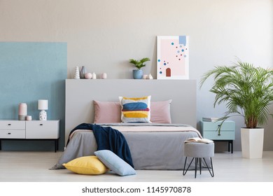 Colorful pillows on grey bed in modern bedroom interior with poster and plants. Real photo