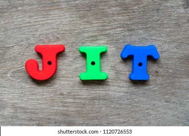 Colorful plastic alphabet in word JIT (Abbreviation of just in time) on wood background