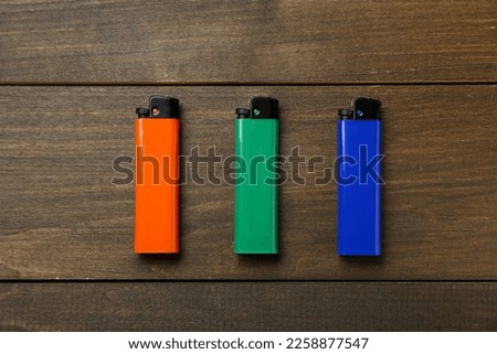 Colorful plastic cigarette lighters on wooden table, flat lay