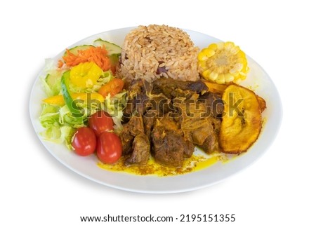 A colorful plate of Caribbean or Jamaican curried goat dinner with rice, corn, plantain and salad isolated on white