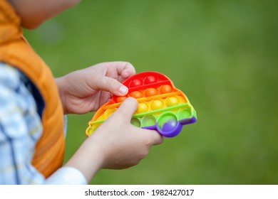 Colorful Popular Fidget Toy Using For Development Of Fine Motor Skills And Mental Health. Kid Playing With Popit Rainbow Toy Trend Of 2021 Year From Tik Tok. Anti Stress Toy For Children With Special