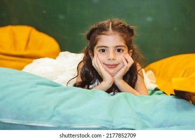 Colorful portrait of little cheerful armenian girl lying and keeping her hands under chin
