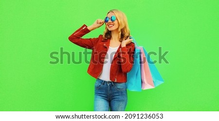 Colorful portrait of stylish happy smiling young woman with shopping bags posing wearing red jacket on green background