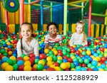 Colorful  portrait of three happy little kids in ball pit smiling happily at camera while having fun in children play center, copy space
