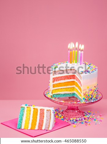 Colorful rainbow Birthday cake with candles over a pink background.
