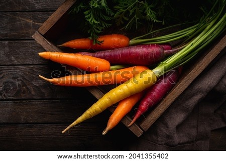 Colorful Rainbow carrot with their green leaves in a box on wooden background, top view