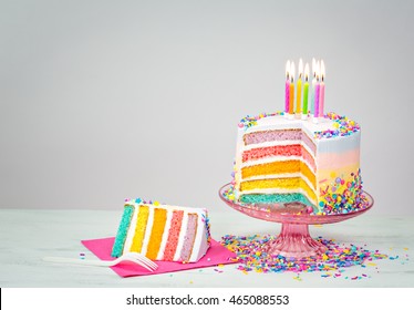 Colorful rainbow layered Birthday cake with lit candles and sprinkles