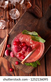 Colorful raspberry soft drink with ice and cinnamon on wooden table, view from above