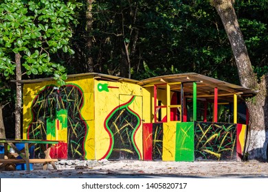 Colorful Rasta Jamaican color vendor shop made of board/wood and zinc roof on tropical Caribbean island white sand beach. Large lush trees give shade outdoors on sunny summer day in Jamaica.