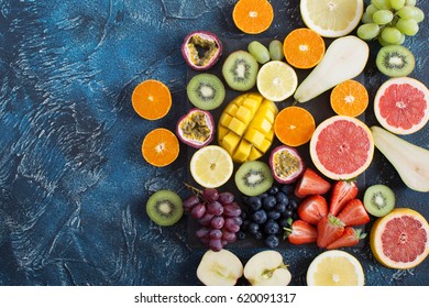 Colorful raw fruits platter: oranges, lemons, kiwis, grapefruits, strawberries, grapes, blueberries, pears, passion fruit, mango on the black slate on the dark blue background, top view - Powered by Shutterstock