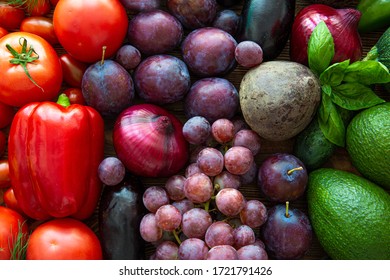 Colorful red, green and violet fruits and vegetables, top view, close up. Tasty fresh tomatoes, paprika, pink grapes and violet plums, green avocado. 