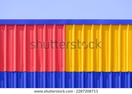 Colorful red, yellow and blue Corrugated Metal Awning Roof against blue Sky background, front view with copy space