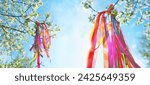 colorful ribbons on blossoming tree in Spring garden, natural background. Symbol of Beltane, Wiccan Celtic Holiday beginning of summer. magic witchcraft, folk traditions, rituals. banner