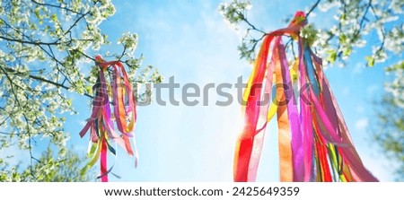 colorful ribbons on blossoming tree in Spring garden, natural background. Symbol of Beltane, Wiccan Celtic Holiday beginning of summer. magic witchcraft, folk traditions, rituals. banner