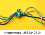 Colorful ropes tied in knot on yellow background, top view. Unity concept