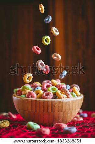 Colorful round fruit cereals falling into a wooden bowl on a red table. Preparing breakfast. 