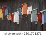 A colorful row of birdhouses attached to a dark wooden wall. Each birdhouse features unique designs and colors, including polka dots and floral patterns, creating a vibrant display.