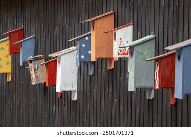 A colorful row of birdhouses attached to a dark wooden wall. Each birdhouse features unique designs and colors, including polka dots and floral patterns, creating a vibrant display. - Powered by Shutterstock