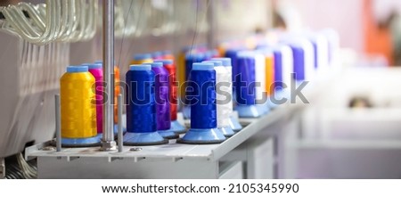 Colorful rows spools of thread stand on embroidery machine in garment industry.