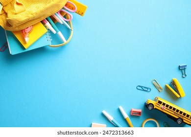 Colorful School Supplies. Flat lay of school items including yellow backpack, notebooks, pencils, markers, a ruler, and a mini school bus on a blue background - Powered by Shutterstock