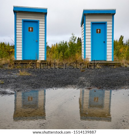 Colorful simple basic outhouses mirrored in big water puddle left from heavy rain