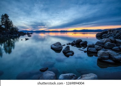 Colorful sky at sunset at Sand Harbor with calm water, beautiful rock formations, and mountains in the background, Lake Tahoe, Carson City, Nevada
