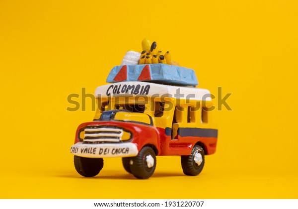 Colorful souvenir toy\
car vehicle with the colors of Colombia. Studio still life toy\
against a seamless yellow background. TRANSLATION: \'COLOMBIA. CUACA\
VALLEY OF CALI\'