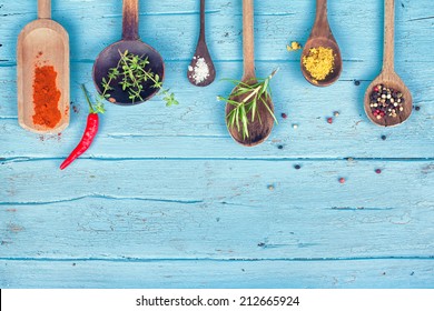 Colorful Spices and herbs on rustic spoons over blue wooden background 