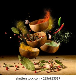Colorful spices and peppers in wooden bowls flying over the table on black background. Spices and seasonings powder splash. Freeze motion photo.