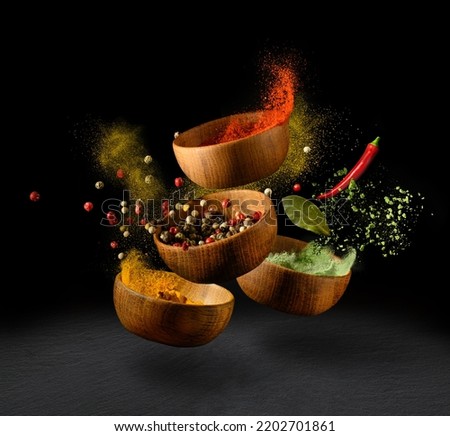 Colorful spices and peppers in wooden bowls flying over black background. Spices and seasonings powder splash. Freeze motion photo.