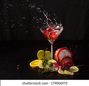 Colorful splash in martini glass from falling lemon, with pomegranate seeds, slices of dragon fruit, green apple, oranges and lemons, on a wet black table
