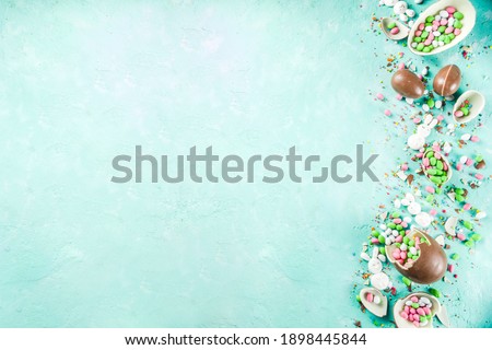 Colorful spring easter sweets background, with chocolate eggs, sugar sprinkles and marshmallow bunny, turquoise light blue concrete background copy space top view
