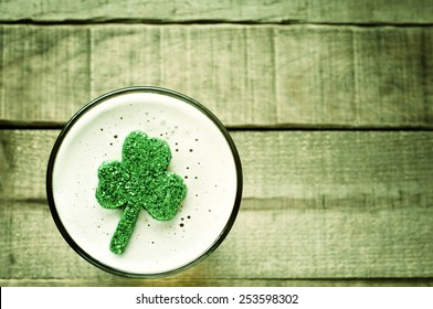 Colorful St. Patricks Day Shamrock Floating In Frothy Beer Mug On Rustic Wood Board Background With Room Or Space For Copy, Text, Your Words.  Horizontal Moody Faded Green Tint, Hue Instagram 