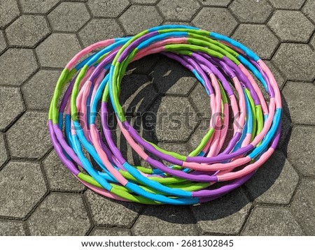 A colorful stack of twisted hula hoops sits on a hexagonal patterned pavement in bright sunlight.
