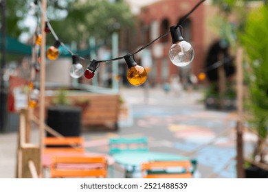 Colorful String Lights Illuminate Outdoor Dining Area in Urban Park During Late Afternoon - Powered by Shutterstock