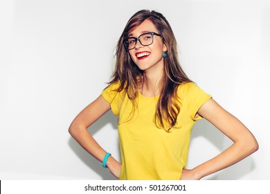 Colorful Studio Portrait of Hipster Fashion Smiling Girl with Hands on Hips at white Background. Fun positive young smart woman in glasses and colorful yellow shirt smiling with perfect teeth.