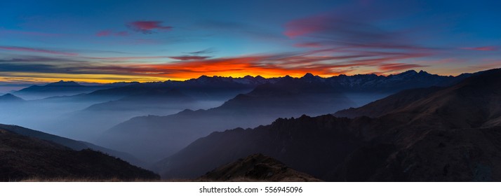 Colorful sunlight behind majestic mountain peaks of the Italian - French Alps, viewed from distant. Fog and mist covering the valleys below, autumnal landscape, cold feeling. - Powered by Shutterstock