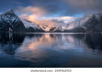 Colorful sunrise illuminates snowy mountains reflecting in the calm water of fjord in Lofoten, Norway. Breathtaking winter landscape. Dramatic scenery with sea, rocks in snow, pink sky with clouds - Powered by Shutterstock