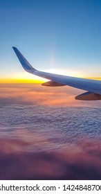 A colorful sunrise seen from the plane window. Sun is raising from the clouds, painting them pink and orange. Horizon line turns yellow with the sunbeams. Plane wing covering the sun. Romantic view - Shutterstock ID 1424848700