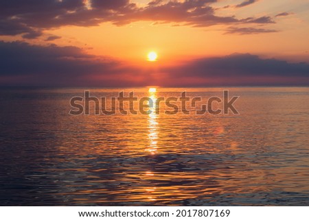 Colorful sunset on the beach. The sun is setting in the sea. Beautiful background image with sunset, clouds and sea.