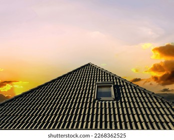 Colorful sunset. Open roof window in velux style with black roof tiles
