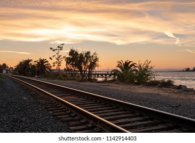 Colorful sunset over a bay with railroad tracks in the foreground and trees, water and clouds in the background - Shutterstock ID 1142914403
