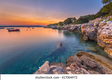 Colorful Sunset Over The Rocky Coast Of Croatia. Long Exposure Image Of Sunset, Rocks, Boats And Turqoise Water On The Island Of Cres.