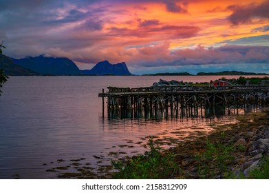 Colorful sunset over a Wooden jetty on Senja Island in Norway with mountains in the background.