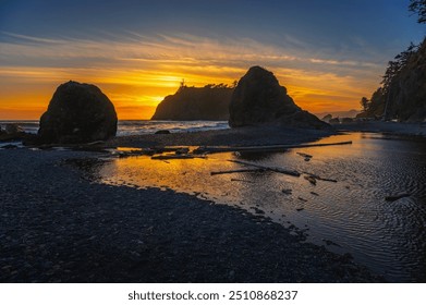 Colorful sunset at Ruby Beach featuring sea stacks silhouetted against the vibrant sky, with tide pools and driftwood on the pebble shoreline in Olympic National Park, Washington state, USA