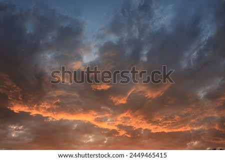 A colorful sunset sky with warm light, showcasing fluffy and wispy clouds in shades of orange, red, and yellow. A mesmerizing scene of natures artistry and peacefulness.