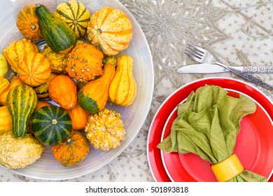 Colorful Thanksgiving Centerpiece With Ornamental Gourds In Different Colors Of Orange And Green Alongside A Matching Place Setting With Orange Plate And Green Napkin, Overhead View