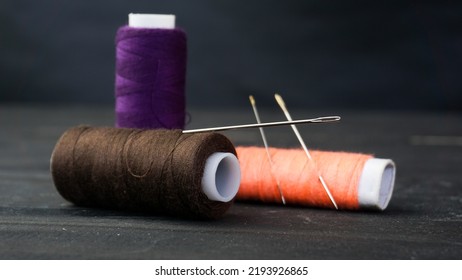 Colorful Thread And Needle As Sewing Equipment For Needlework On Wooden Black Background. Tailor Accessories