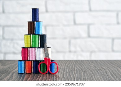 Colorful threads and scissors ordered as pyramid on the wooden table. Embroidery and textile industry background. Copy space for text